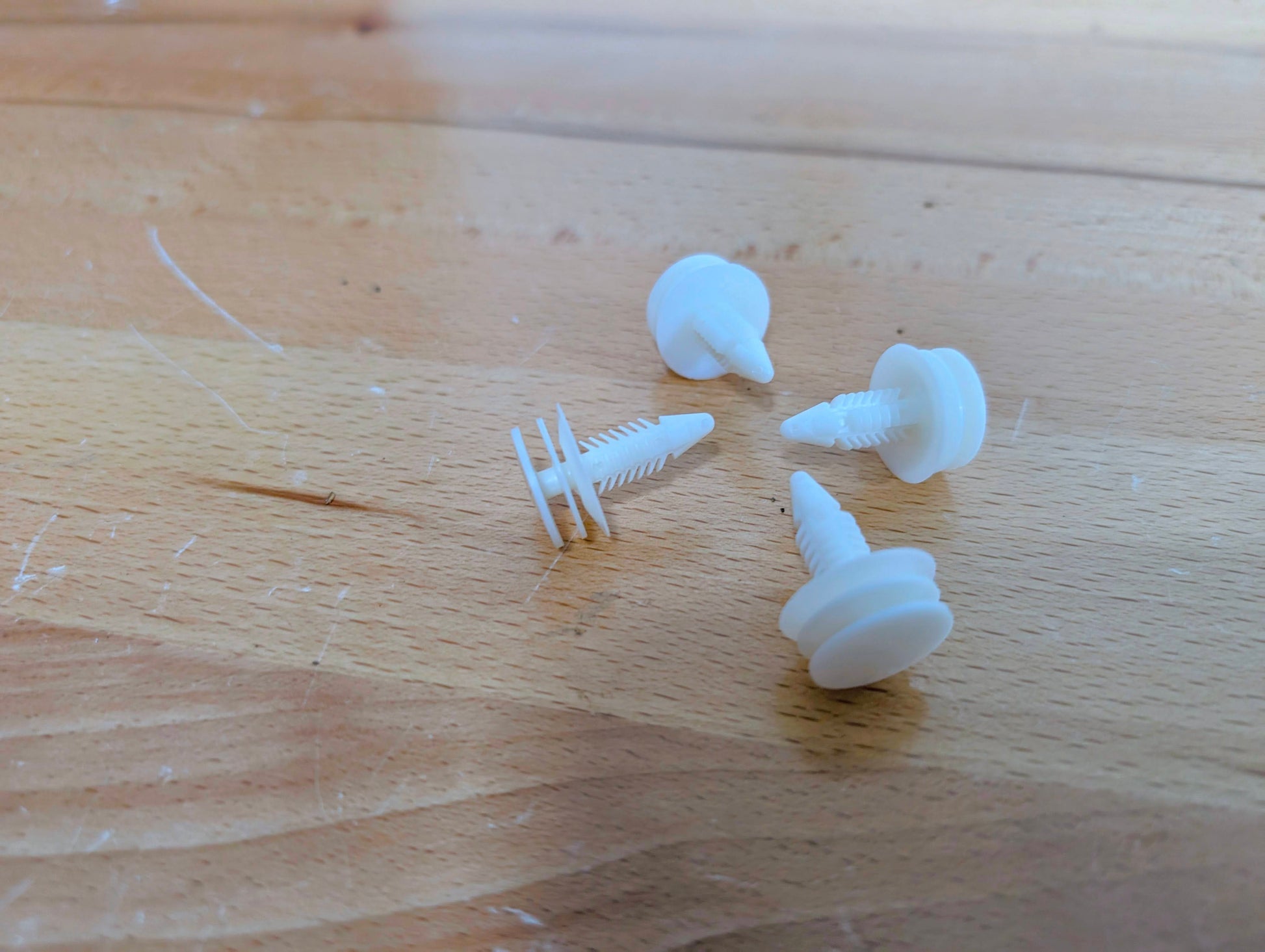 Four white plastic clips from The Ugly Truckling KIT Door Panel Armrest Repair w/Clips for 1998-2005 Chevy S10, Blazer, GMC Sonoma, and Jimmy rest on a lightly scratched wooden surface.