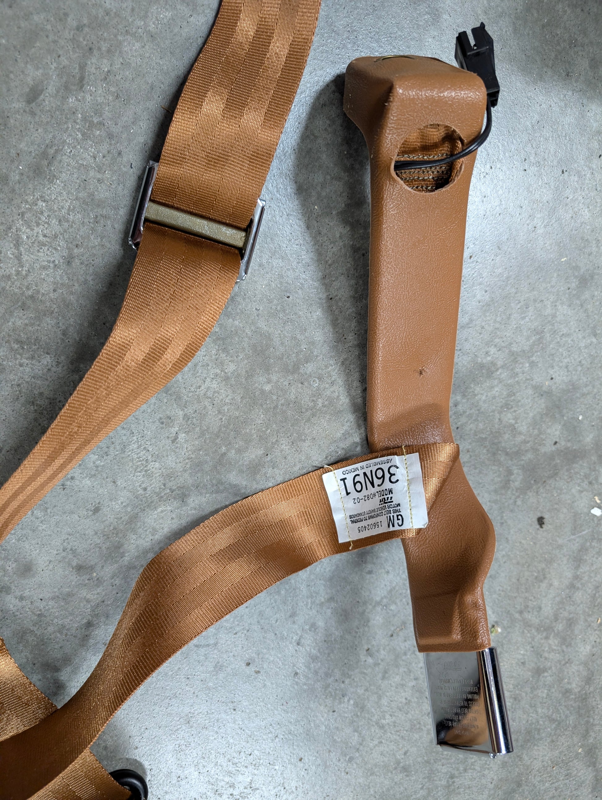 A Brown NOS General Motors passenger seat belt retractor & buckle for 1982–1993 Chevy S10/GMC S15, shown on gray concrete. A white GM label (39691) is attached—ideal Chevrolet S10 or GMC S15 seat belt replacement.