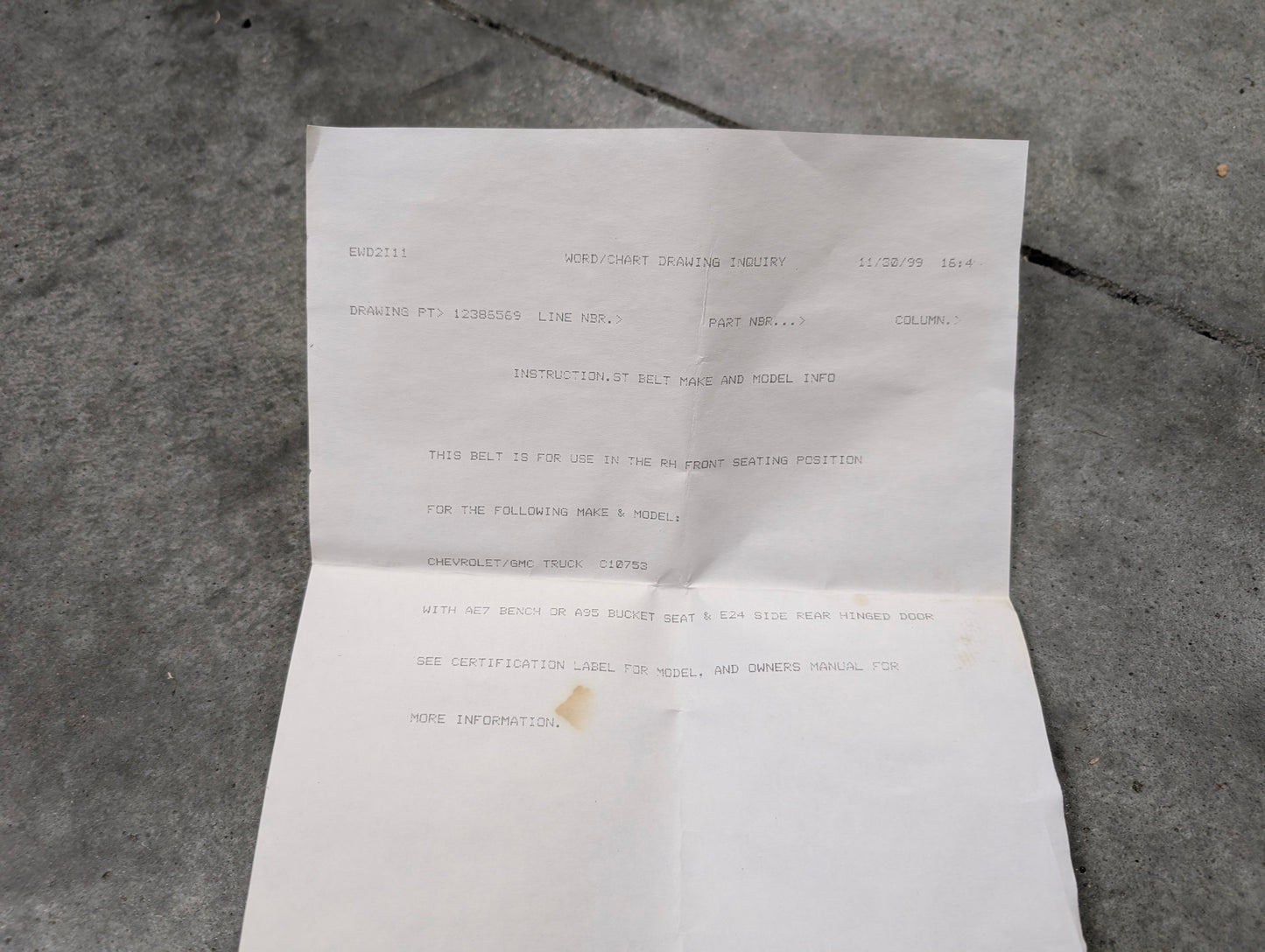 An unfolded white sheet with typed instructions for the NOS Passenger Seat Belt Retractor & Buckle in Blue for 1988-1994 Chevy/GMC C/K Trucks by General Motors lies on concrete, its edges slightly crumpled.
