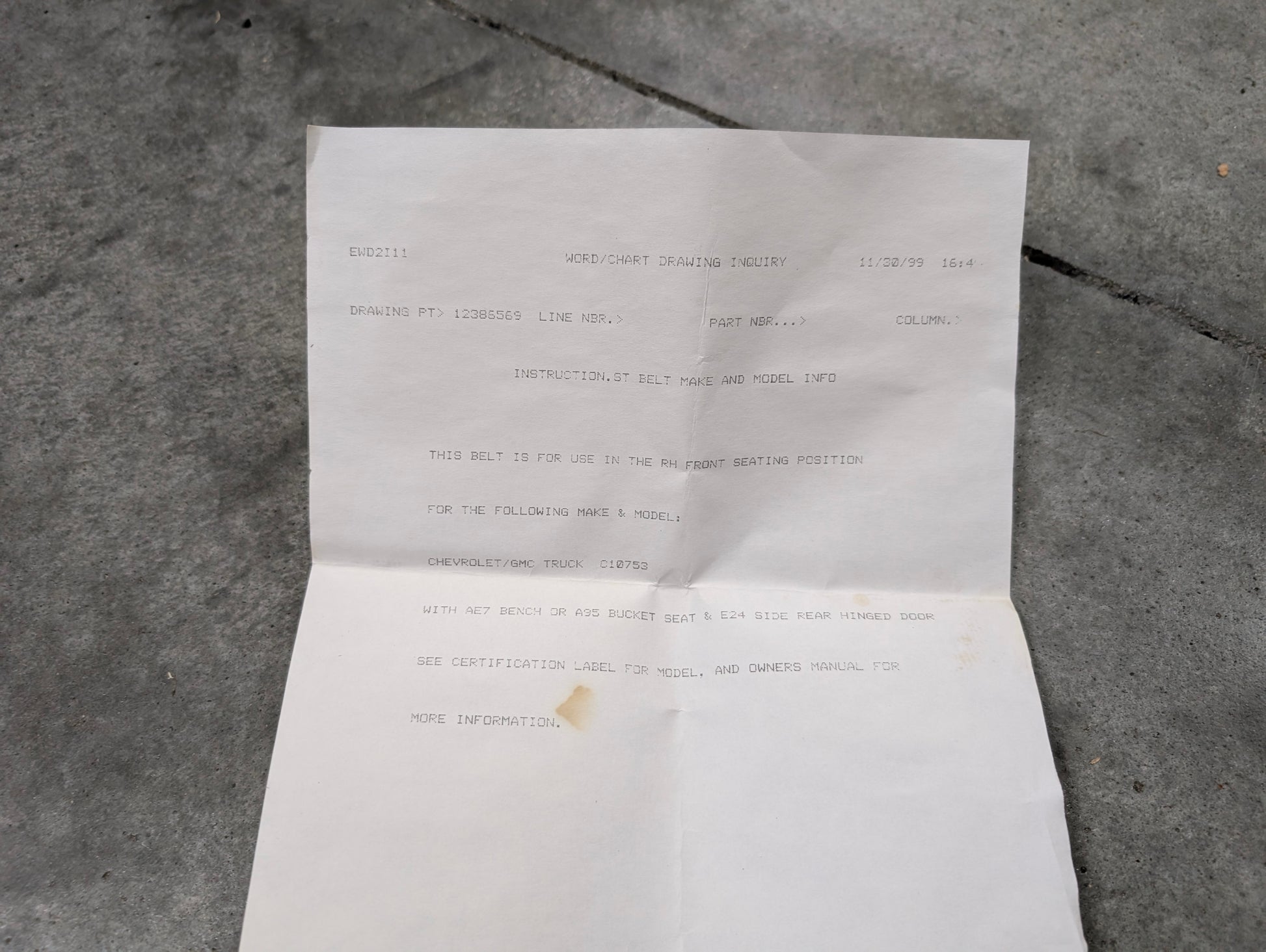 An unfolded white sheet with typed instructions for the NOS Passenger Seat Belt Retractor & Buckle in Blue for 1988-1994 Chevy/GMC C/K Trucks by General Motors lies on concrete, its edges slightly crumpled.