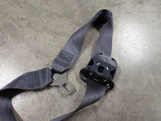 A blue General Motors NOS passenger seat belt retractor and buckle for 1988-1994 Chevy/GMC C/K trucks lies on a smooth concrete floor.