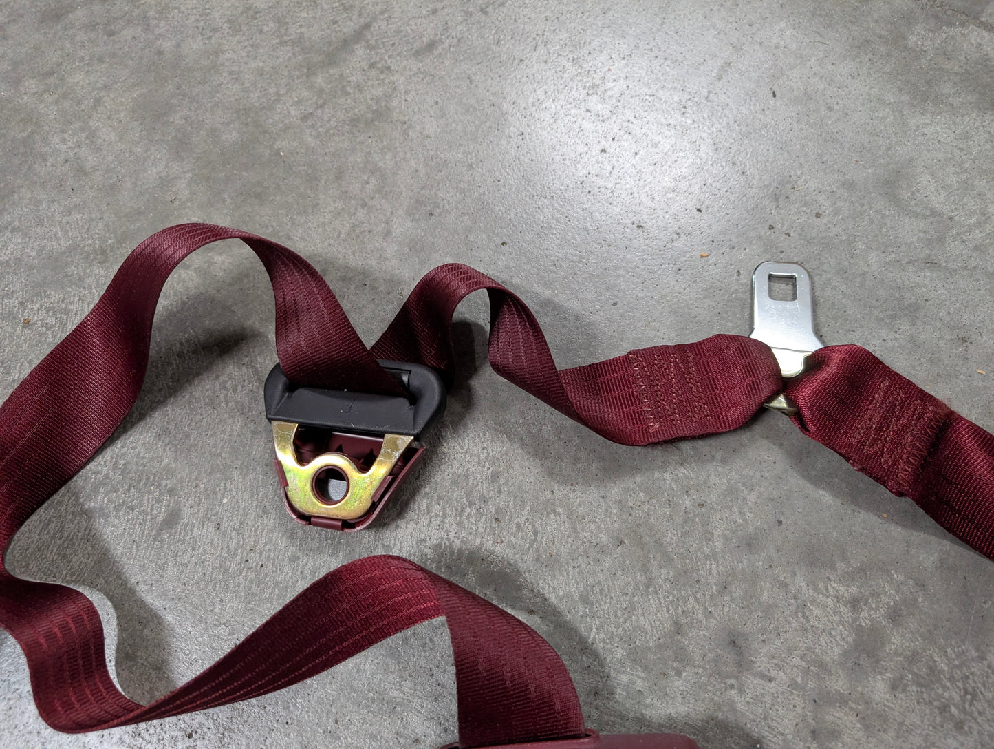 A General Motors NOS red driver bucket seat belt retractor & buckle for 1988-1994 Chevy/GMC C/K trucks is lying on a gray concrete floor.