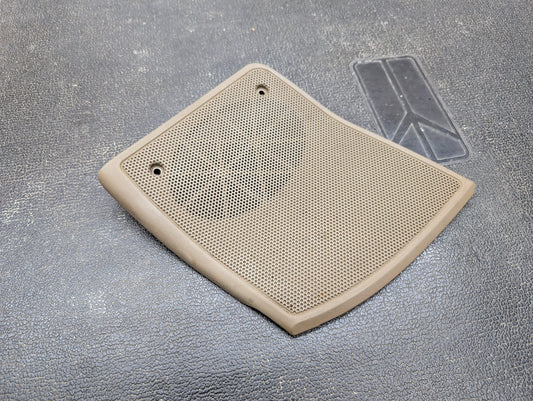 A General Motors OEM beige/tan passenger RH dash speaker grille cover for 1995-1997 Chevrolet S10, Blazer, and more, with two screw holes, lies on a textured black surface. A faint rectangular mark is visible nearby.