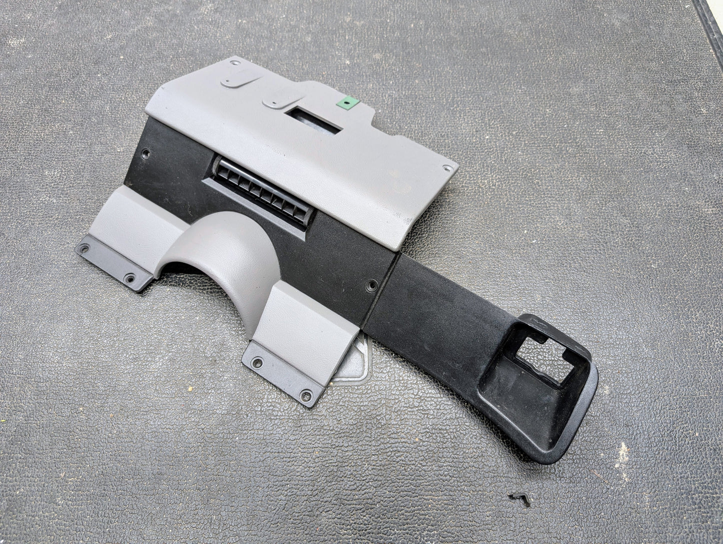A General Motors OEM Lower Dash Trim Knee Bolster in Lt Gray for 1986-1993 Chevy S10 Blazer/GMC S15, featuring a vent opening and contours, is shown on a textured black surface.