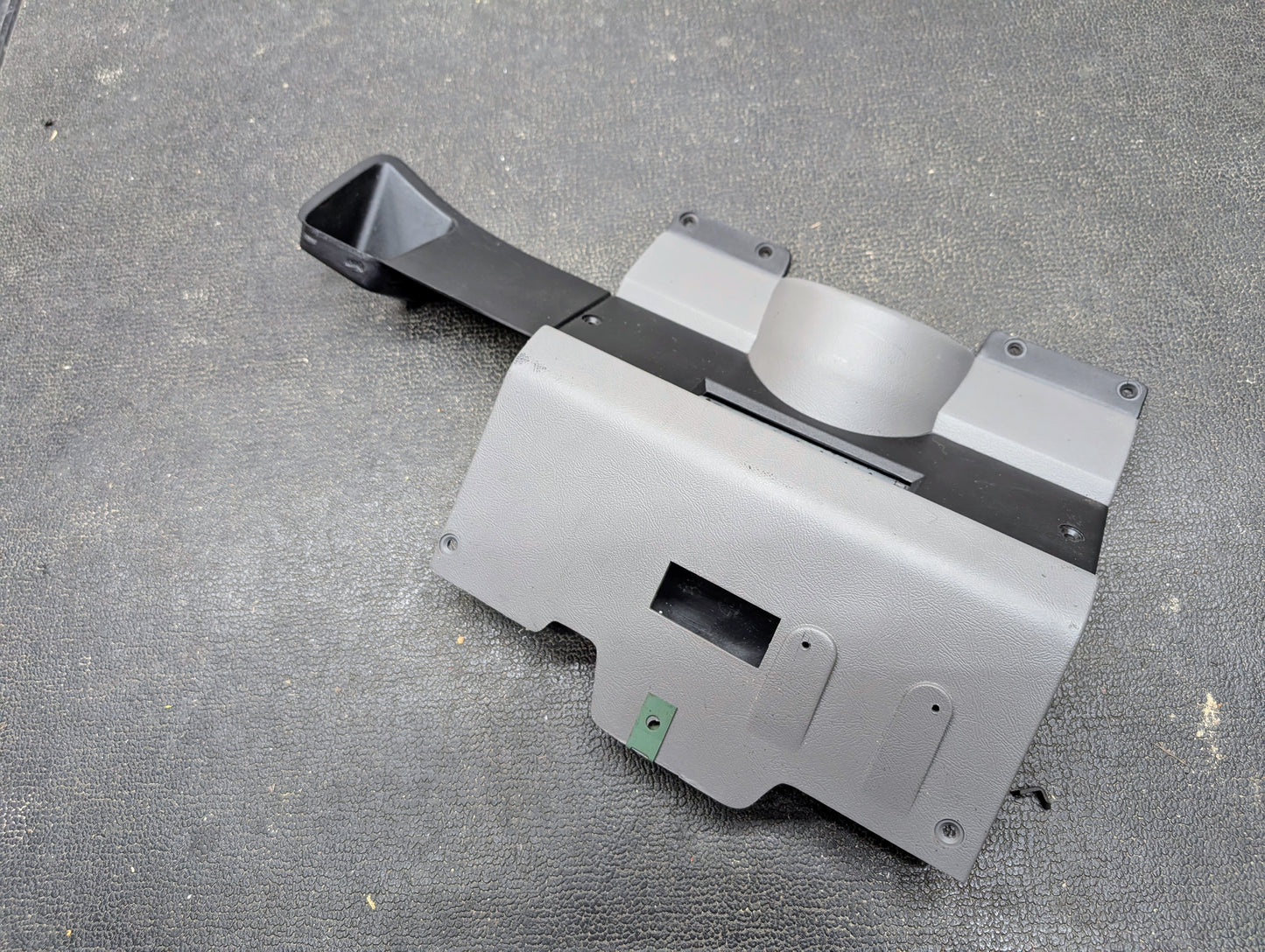 A General Motors OEM Lower Dash Trim Knee Bolster in Lt Gray for 1986-1993 Chevy S10 Blazer and GMC S15, featuring vent openings, mounting holes, and a black duct, shown on a textured black surface.