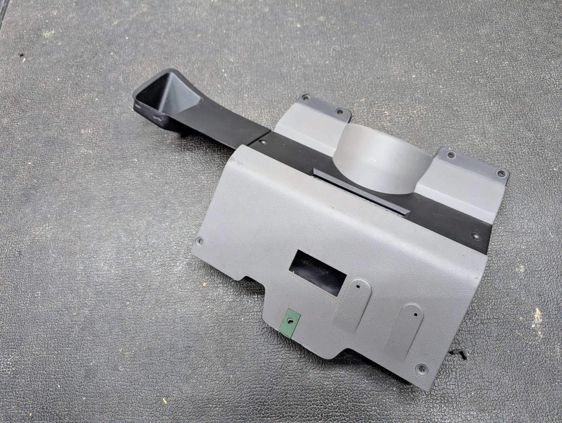 A General Motors OEM Lower Dash Trim Knee Bolster in Lt Gray for 1986-1993 Chevy S10 Blazer and GMC S15, featuring vent openings, mounting holes, and a black duct, shown on a textured black surface.