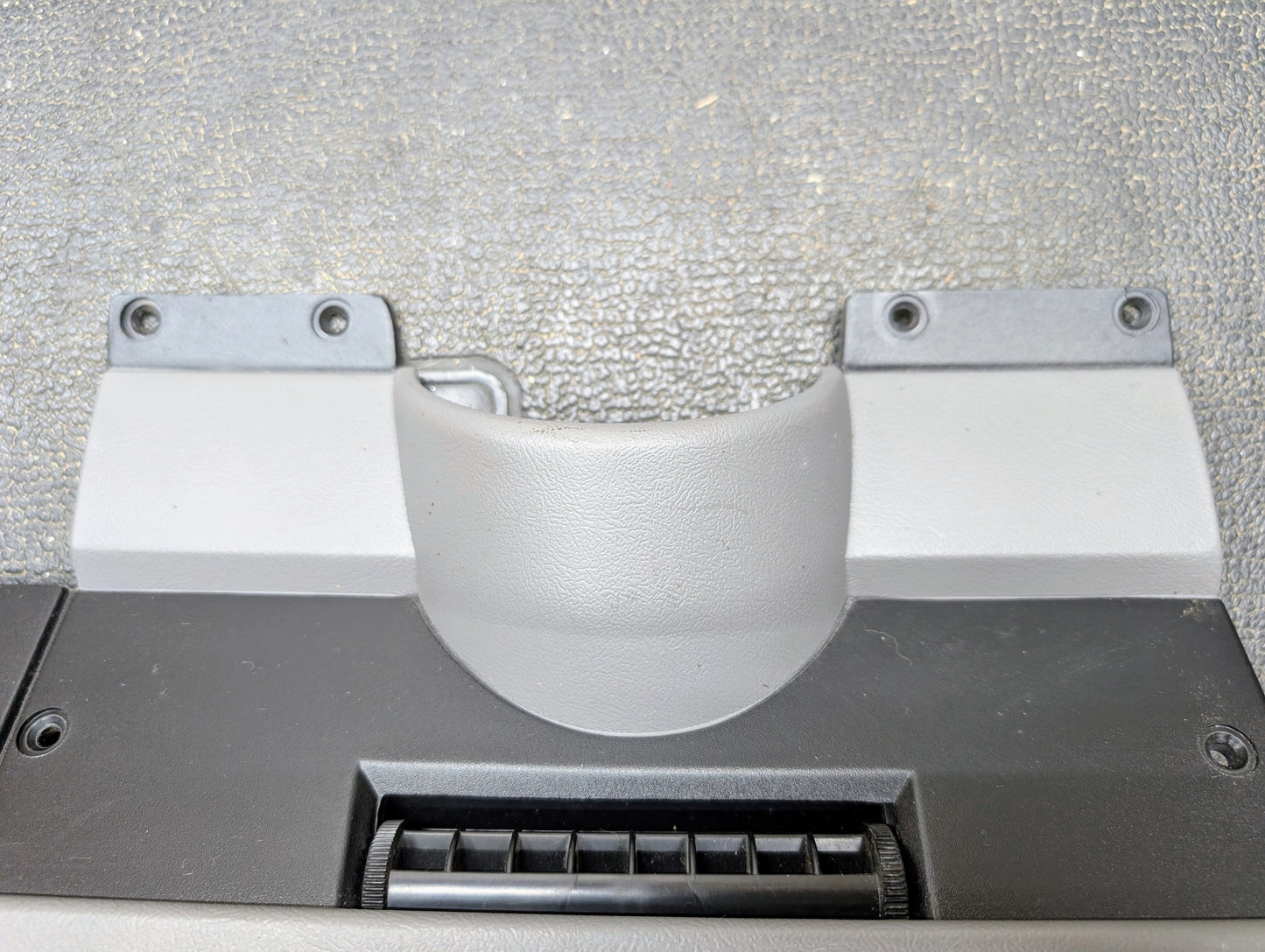 Close-up of a textured OEM Lower Dash Trim Knee Bolster in Lt Gray for 1986-1993 Chevy S10 Blazer GMC S15 by General Motors, featuring a vent below and two metal brackets with screw holes above, plus a rough, speckled finish.
