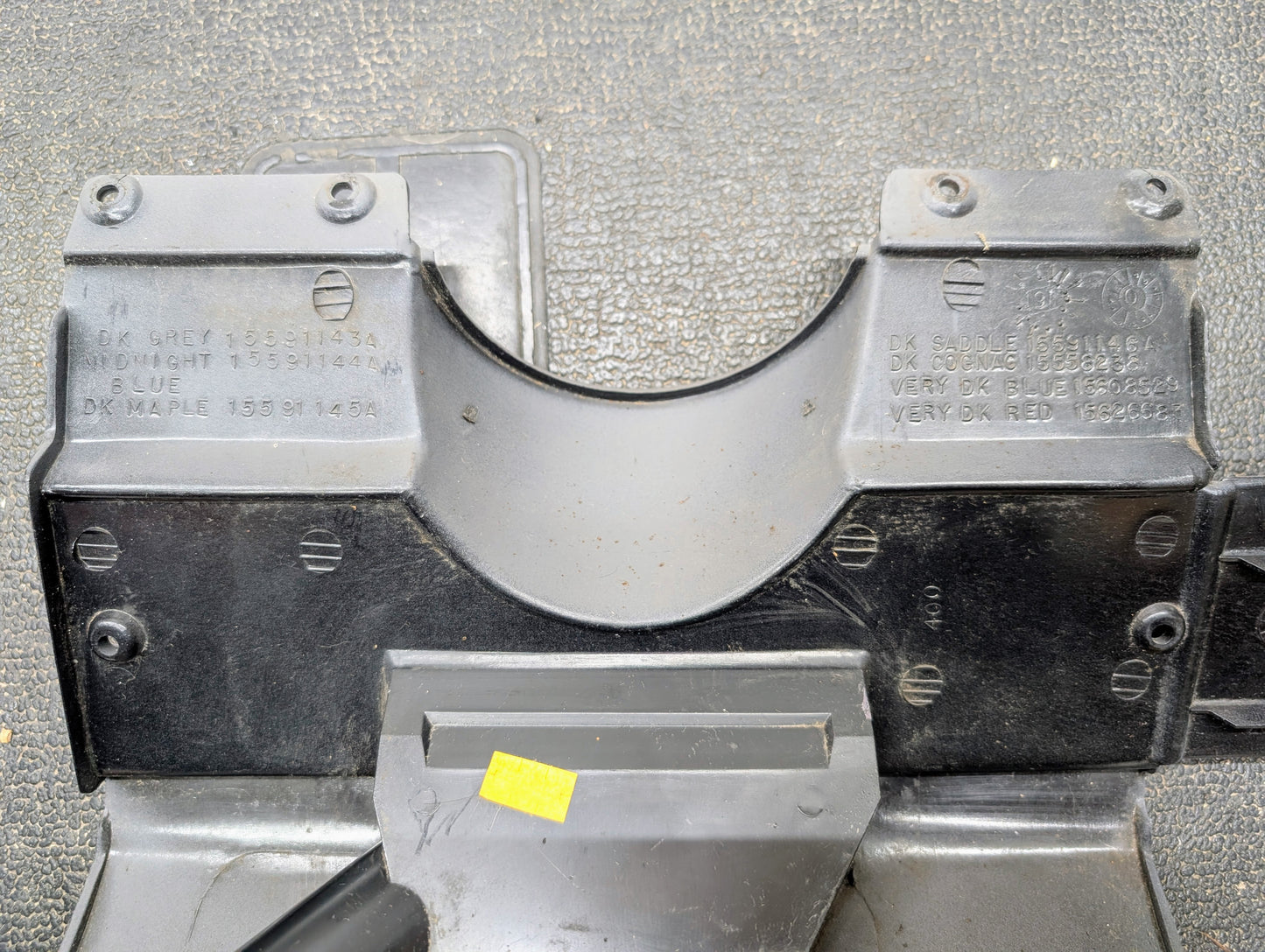 Close-up of a General Motors OEM Lower Dash Trim Knee Bolster in Lt Gray for 1986-1993 Chevy S10 Blazer and GMC S15, showing indented text with color codes, on a textured surface. A small yellow sticker appears near the bottom center.