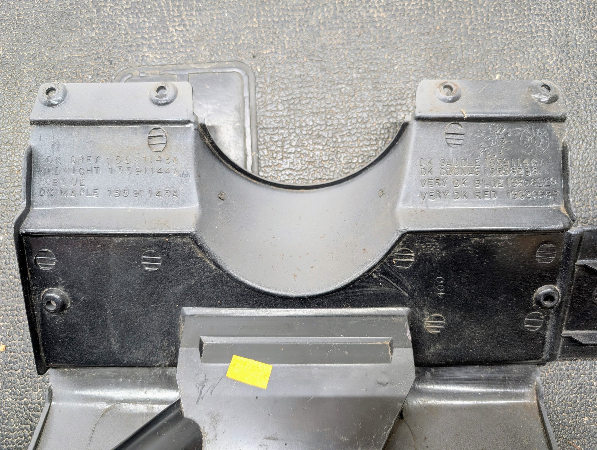 Close-up of a General Motors OEM Lower Dash Trim Knee Bolster in Lt Gray for 1986-1993 Chevy S10 Blazer and GMC S15, showing indented text with color codes, on a textured surface. A small yellow sticker appears near the bottom center.