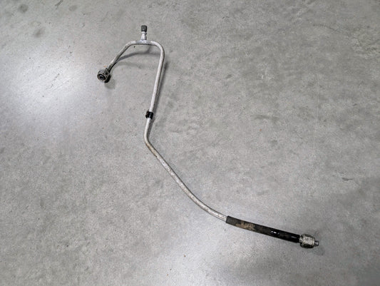 A General Motors OEM Air Conditioning AC High Pressure Hard Line for 1988-1993 2.8L V6 Chevy S10 and Blazer lies on a smooth gray floor, its bent metal tube with a black section—a vital part for HVAC repair.