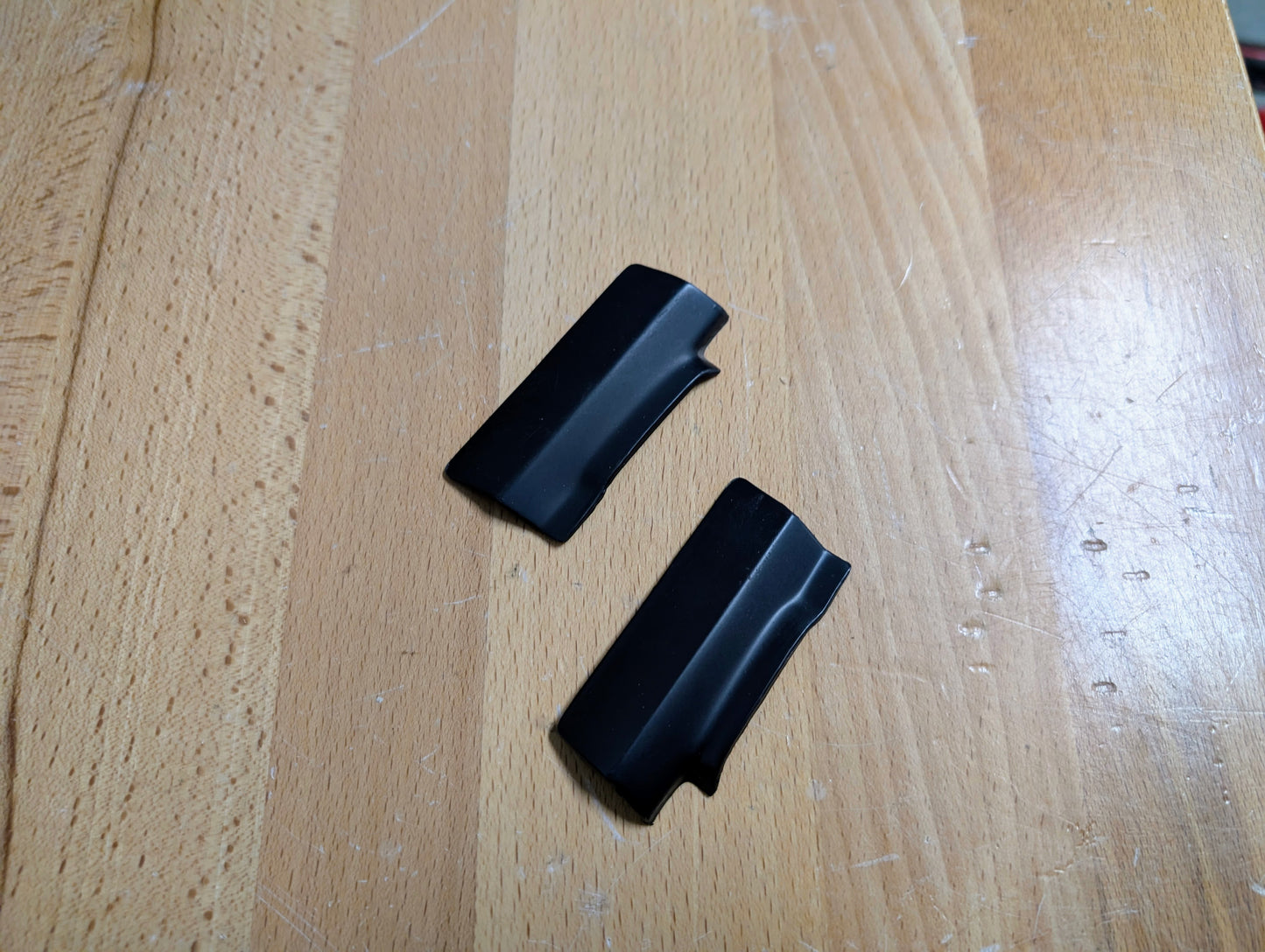 Two small, black, curved rectangular General Motors NOS rear window molding trim panel covers for 1991–1994 Chevy S10, Blazer, GMC S15 Jimmy, and more rest on a light wooden surface.