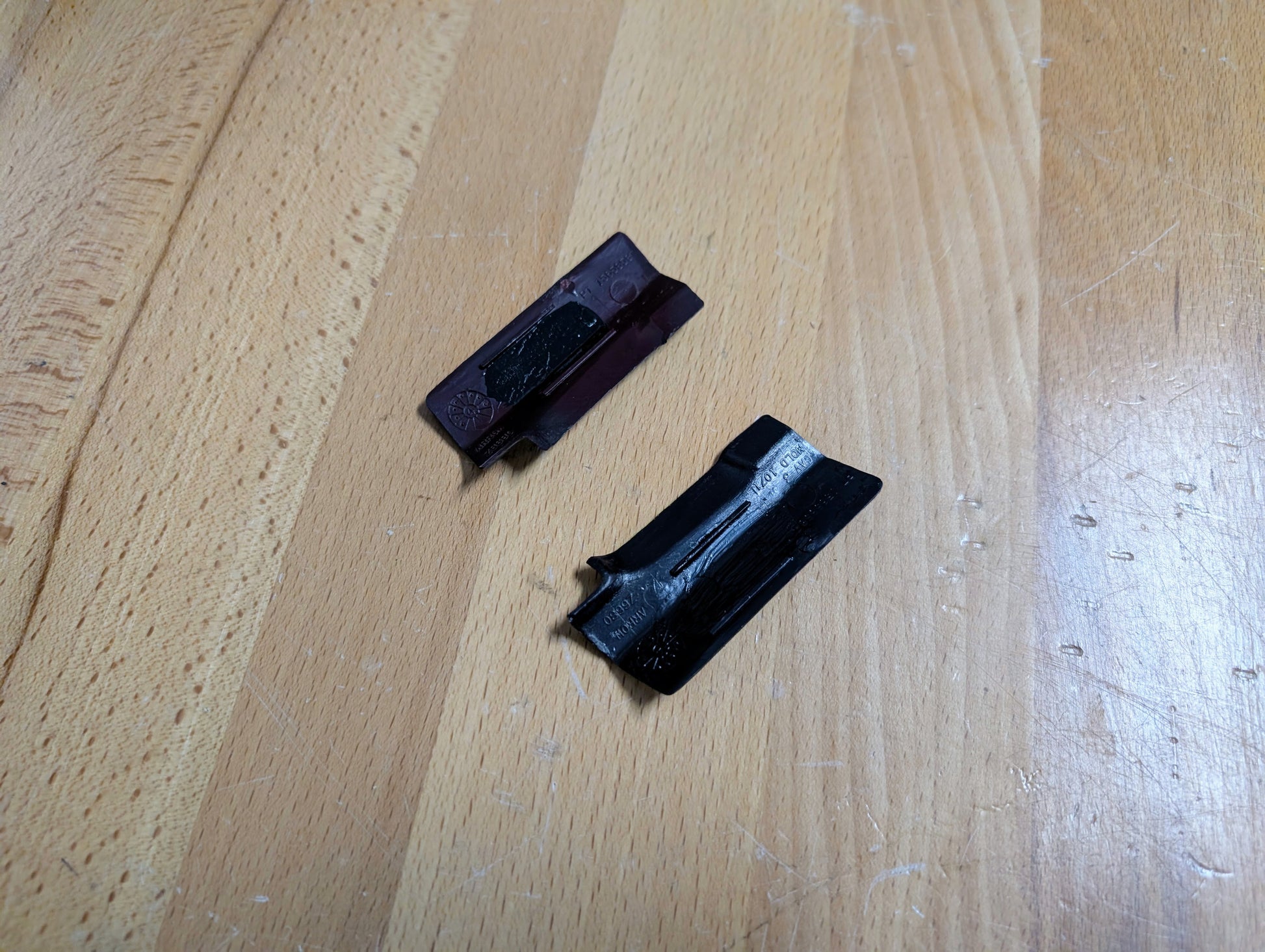 Two broken razor blade cartridges, one dark purple and one black, rest on a light wooden surface next to a General Motors NOS Pair Rear Window Molding Trim Panel Cover for 1991-1994 Chevy S10, Blazer GMC S15 Jimmy, and more.