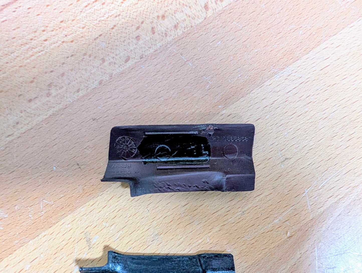 A NOS Pair of General Motors Rear Window Molding Trim Panel Covers for 1991-1994 Chevy S10, Blazer, GMC S15 Jimmy, and more rests on a light wooden surface, one partially in view with textured grip and engraved markings.