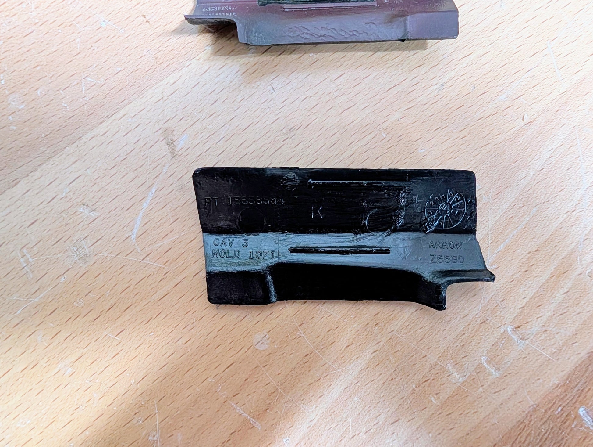 A dark metal object with engravings (CAV 3, MOLD 1071, ARROW, Z889D) rests on wood. It’s a General Motors NOS rear window molding trim panel cover for 1991-1994 Chevy S10, Blazer, GMC S15 Jimmy, and more.