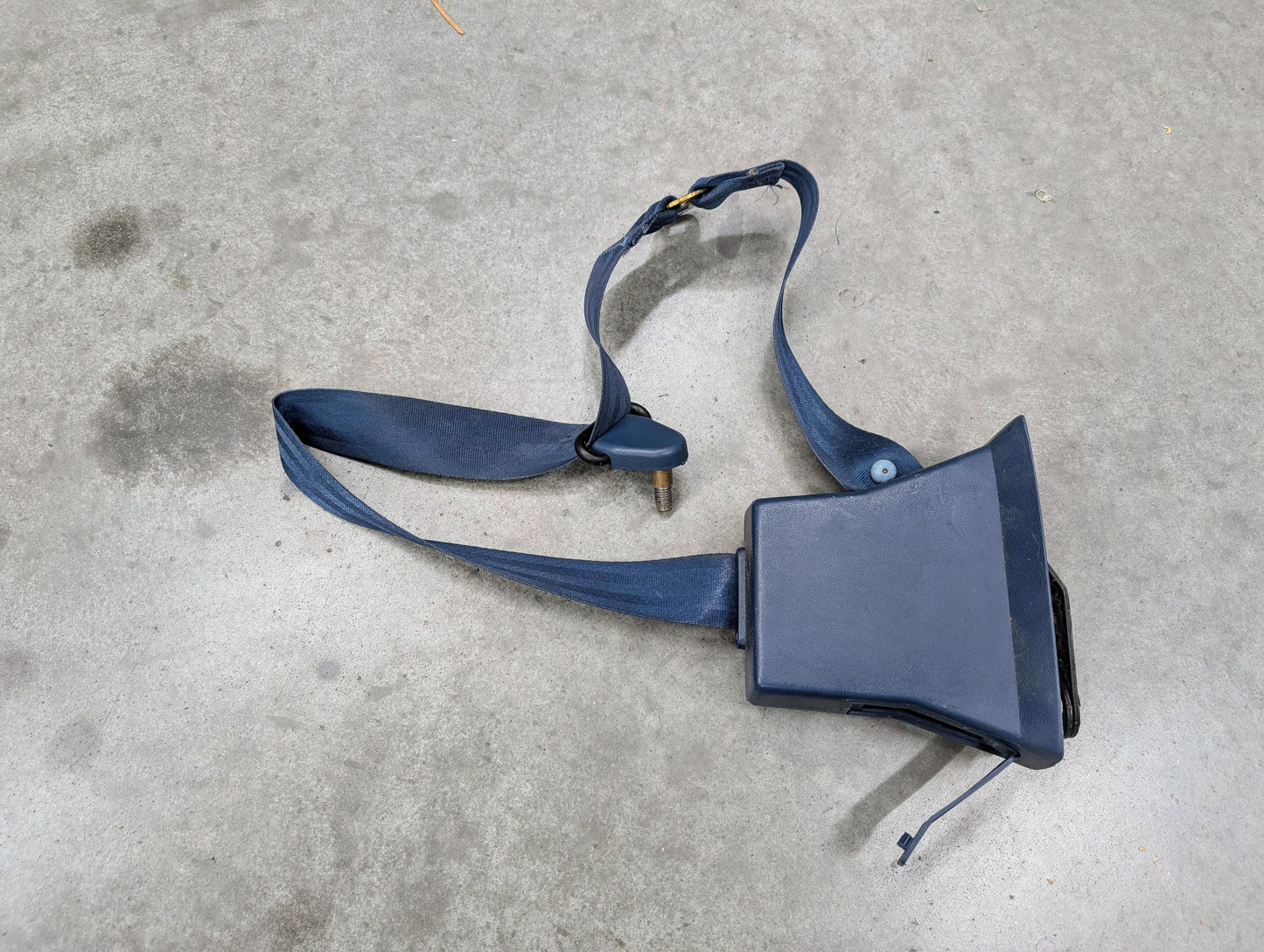 A General Motors OEM blue driver seat belt retractor and buckle for 1982-1993 Chevy S10/GMC S15 is lying uninstalled on a gray concrete floor.