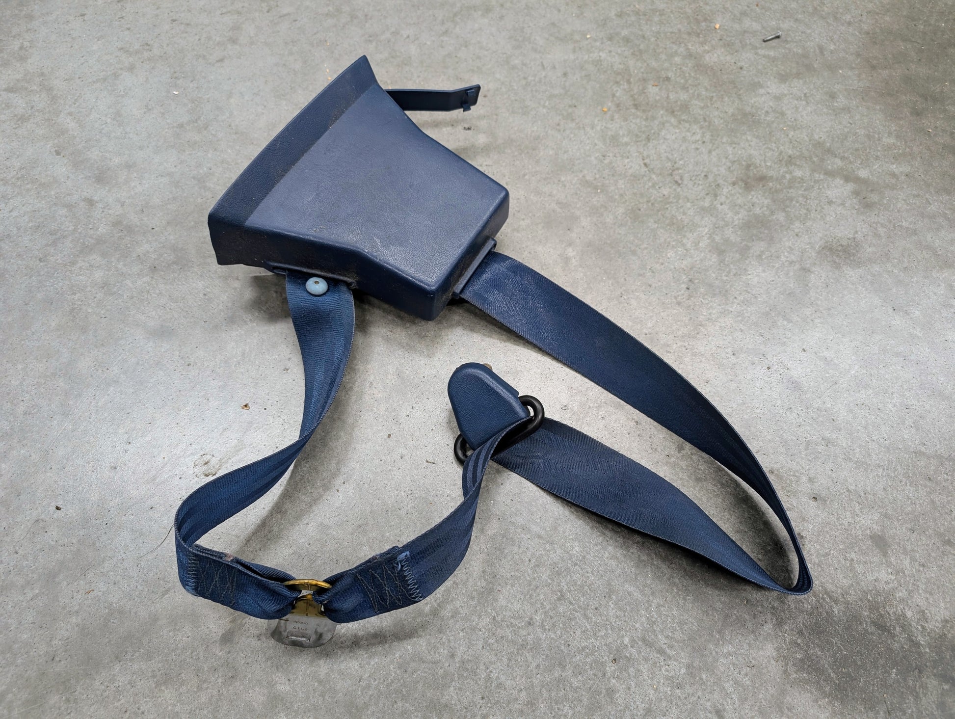 A General Motors OEM driver seat belt retractor and buckle in blue for 1982–1993 Chevy S10 and GMC S15 is lying on a gray concrete surface.